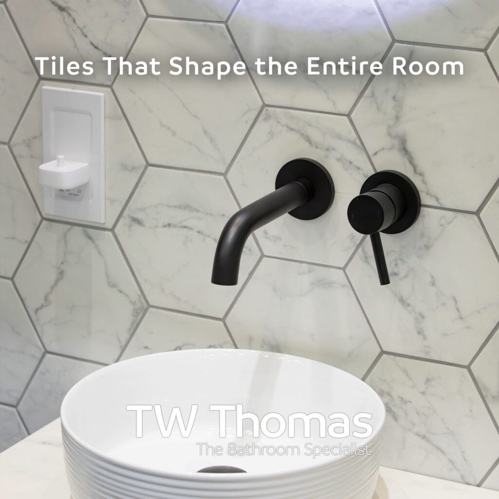 White marble-effect hexagon wall tiles behind a round countertop basin and matt black wall-mounted mixer, captioned Tiles That Shape the Entire Room