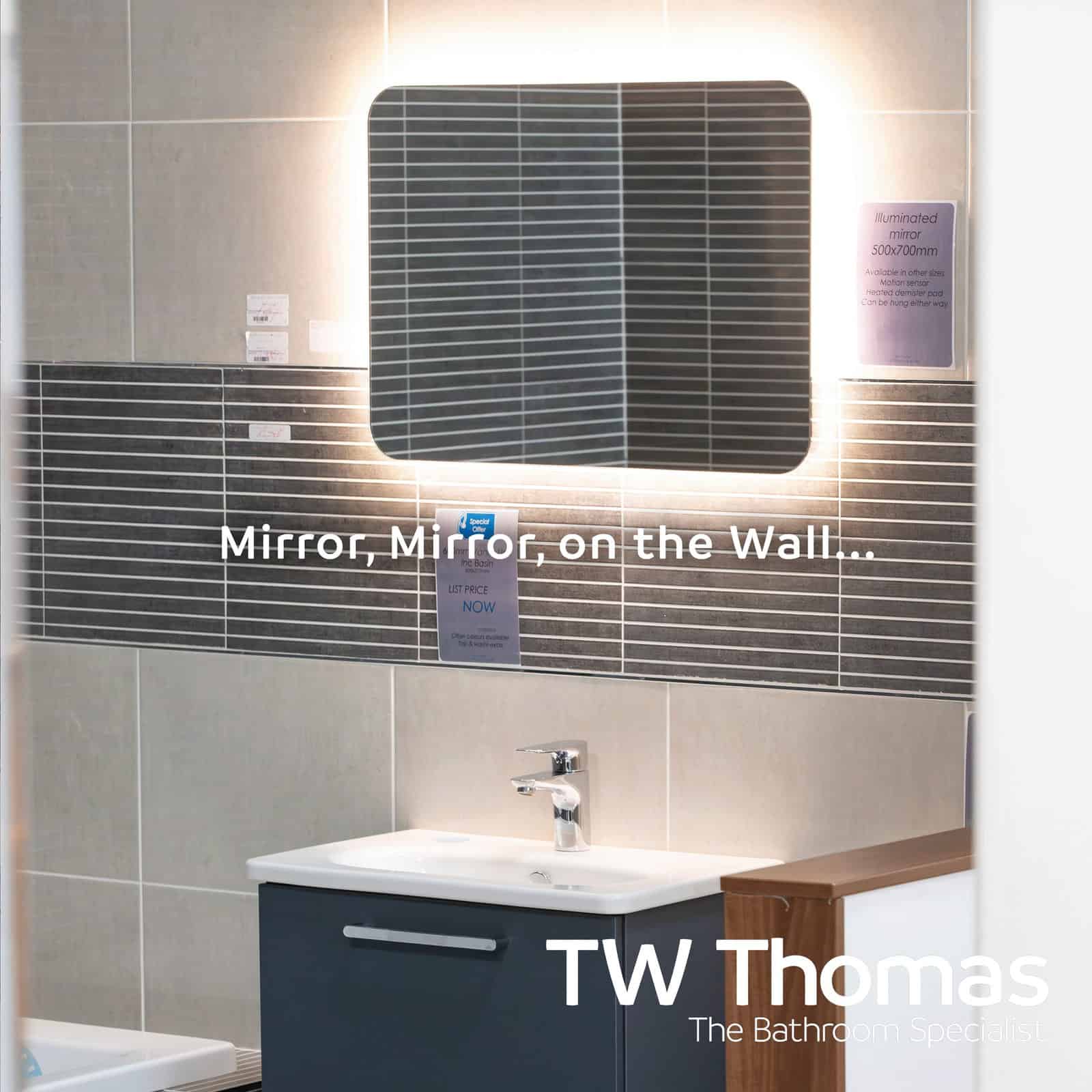 An illuminated rectangular mirror above a dark blue wall-hung vanity and basin, against dark linear mosaic tiles, captioned Mirror, Mirror, on the Wall