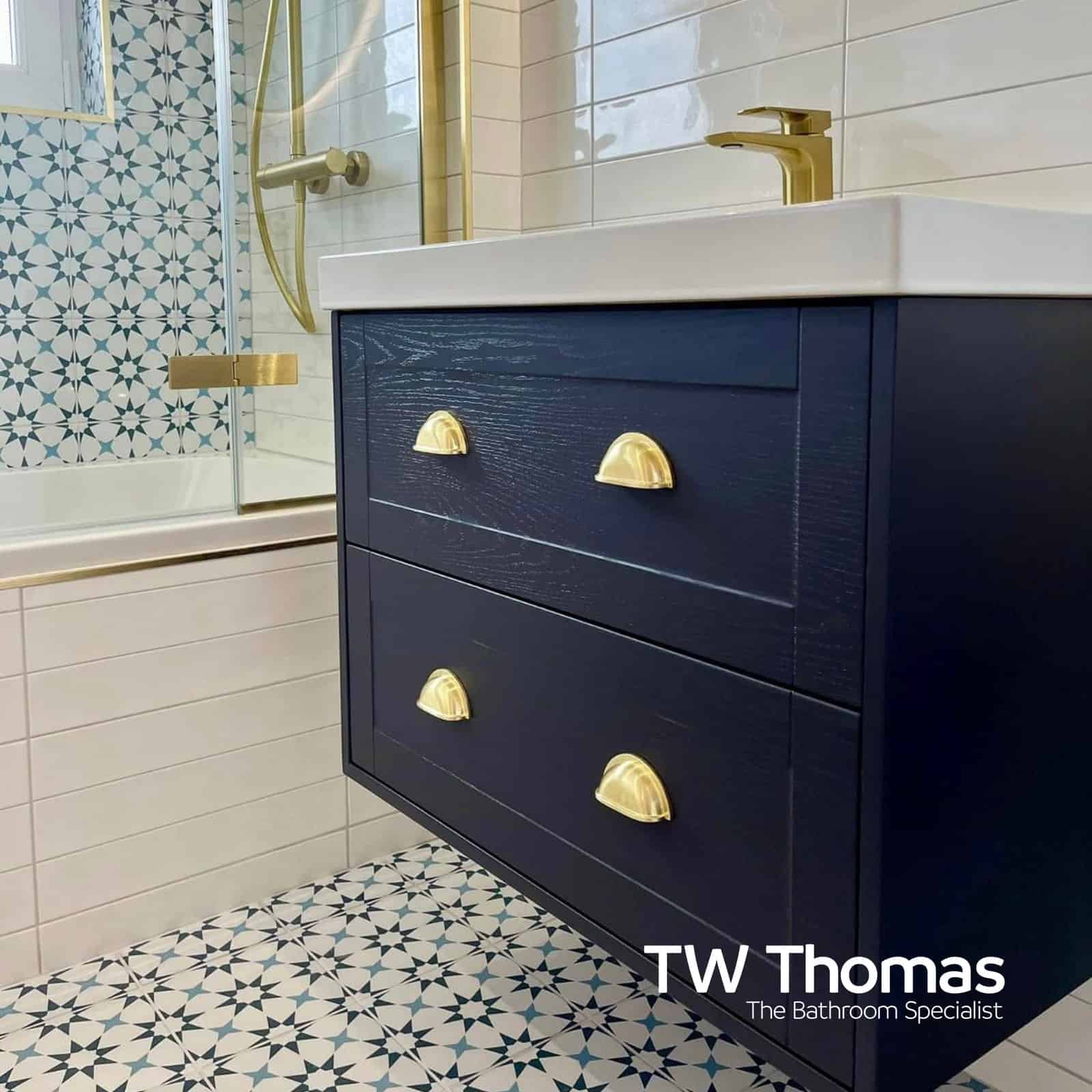 A navy wall-hung vanity with brass cup handles and a white countertop basin, against teal star-patterned wall and floor tiles