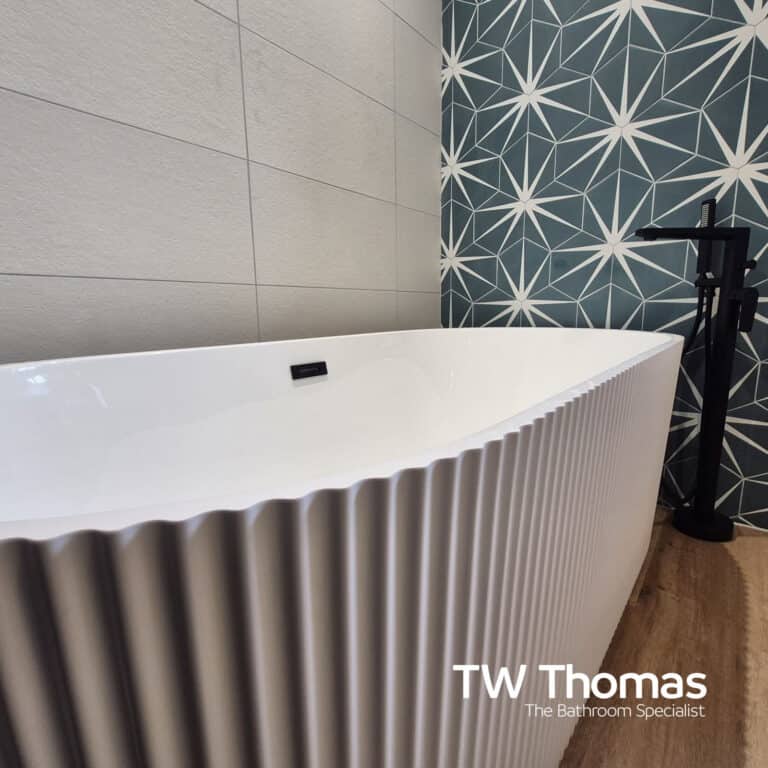 A white fluted freestanding bath against a teal star-patterned wall, with a matt black floor-standing bath filler on a wood-effect floor