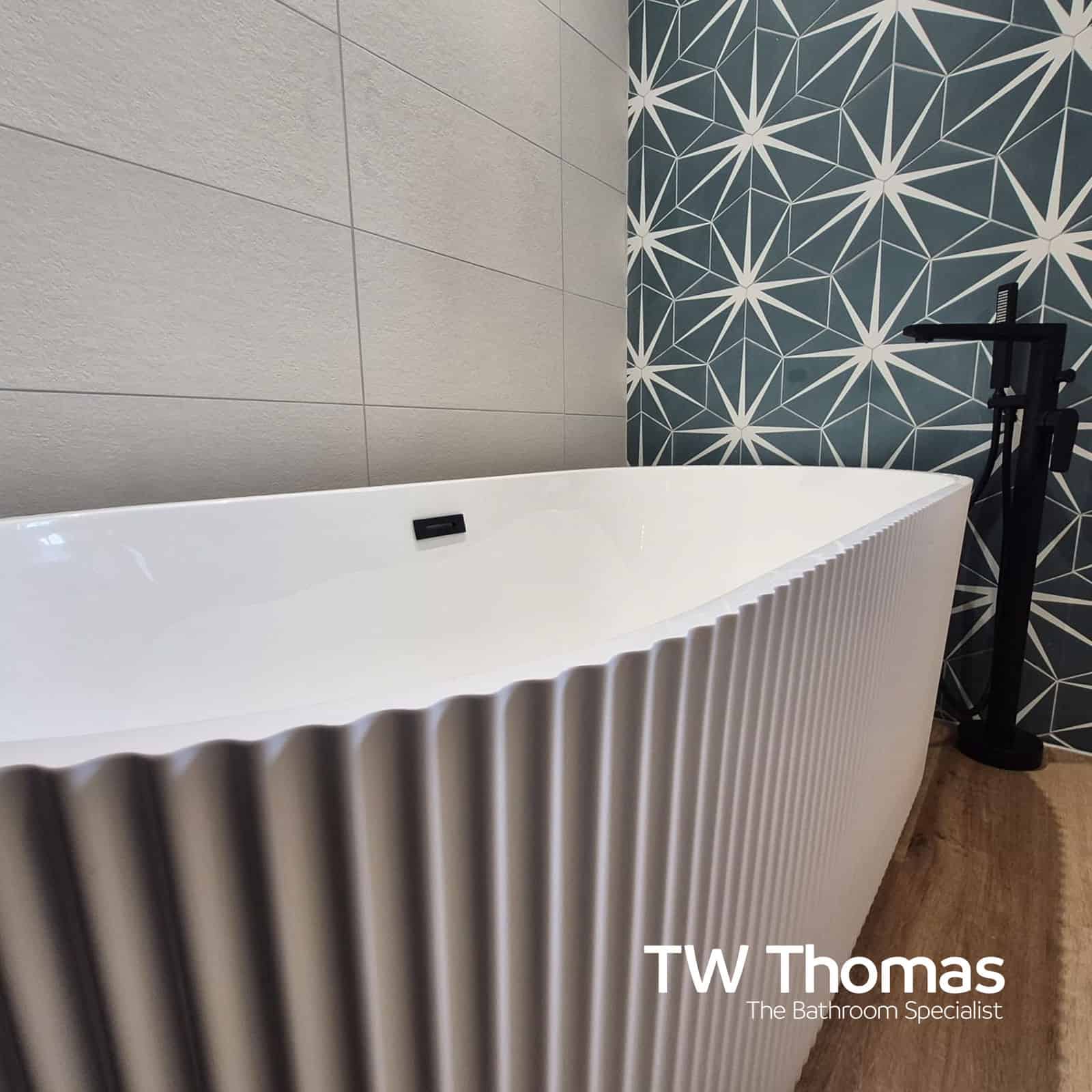 A white fluted freestanding bath against a teal star-patterned wall, with a matt black floor-standing bath filler on a wood-effect floor