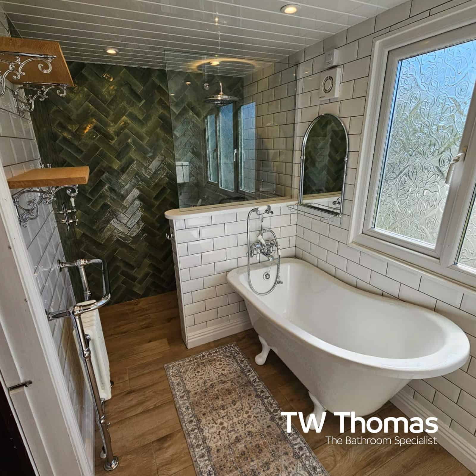 A traditional roll-top bath with a chrome telephone bath and shower mixer, white metro tiles and a dark green herringbone feature wall