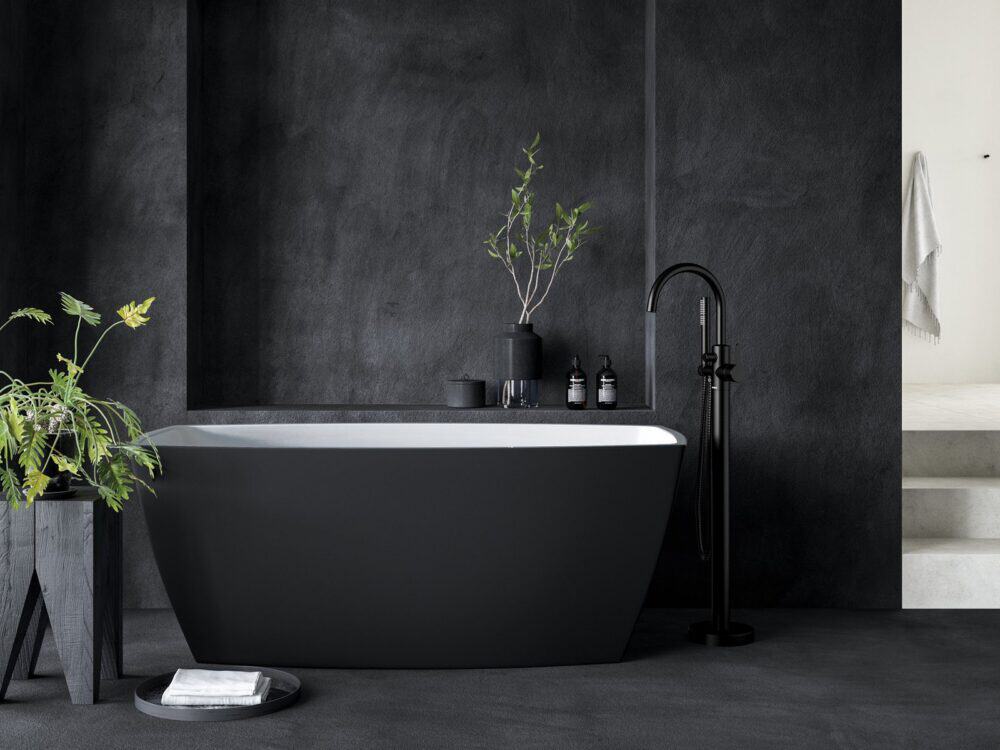 Adamsez matt black freestanding bath against a dark plaster wall with a matt black floor-standing mixer and planting