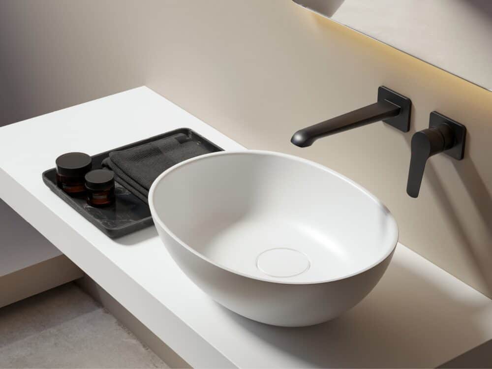 Adamsez AdCast Stone countertop wash basin on a slim white top with a matt black wall-mounted mixer below a lit mirror