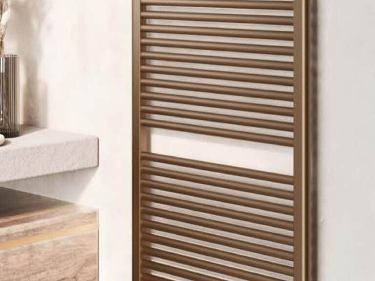 Aqualla towel warmer in brushed bronze on a stone wall beside a timber shelf