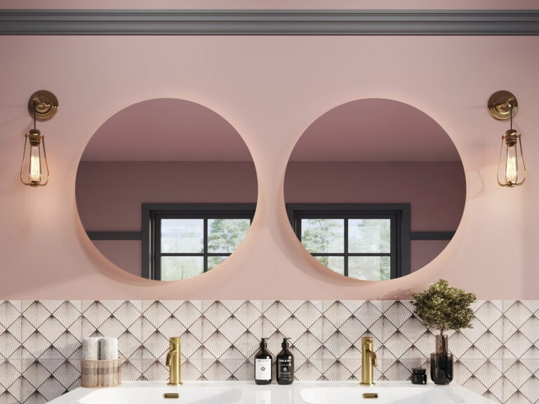 Two Armera round backlit mirrors on a pink wall above a double vanity with brushed gold taps and patterned tiles