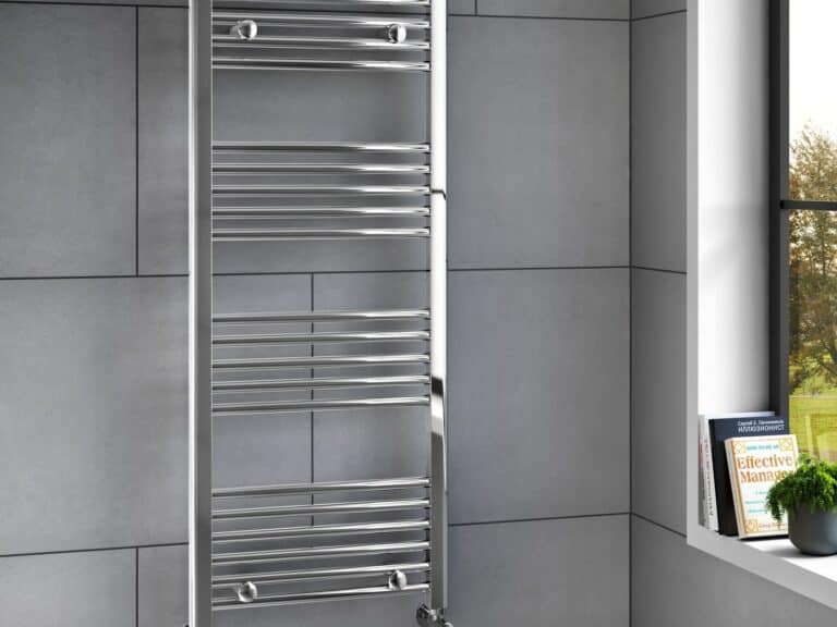 Chrome heated towel rail on a grey tiled wall by a window