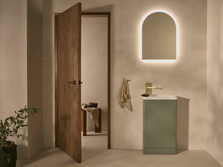 Arched illuminated mirror above a sage green cloakroom basin unit