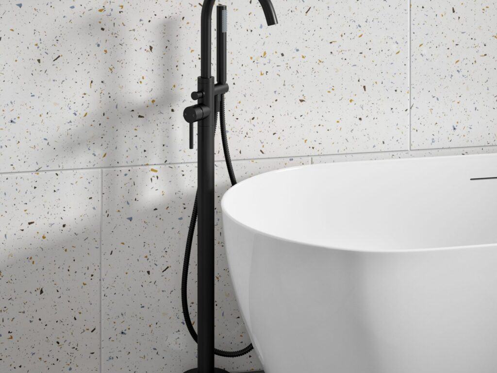 Black floor-standing bath shower mixer beside a freestanding bath