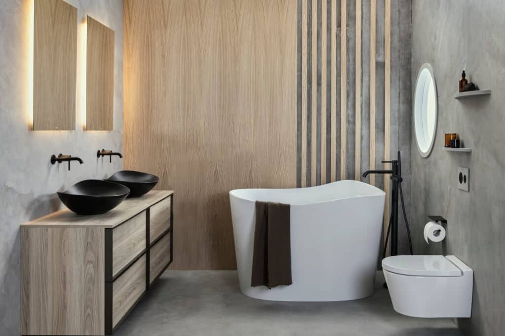 Roca Ohtake freestanding bath, timber double vanity with black countertop basins and a wall-hung WC in a concrete and slatted-timber bathroom