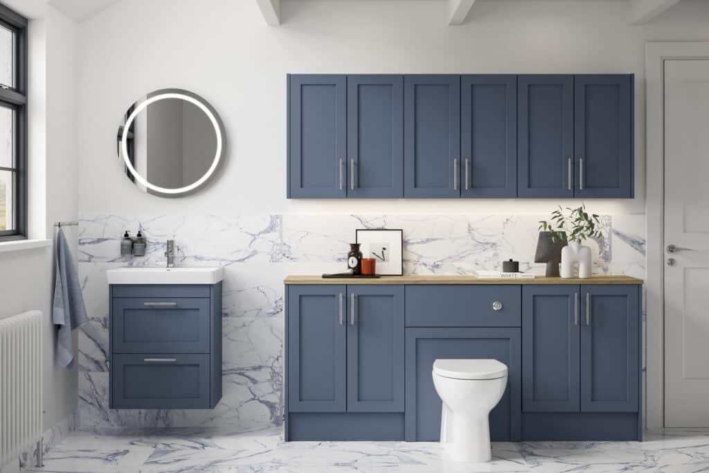 Veldeau Winson muted blue shaker fitted bathroom furniture with an oak worktop, round illuminated mirror and marble wall