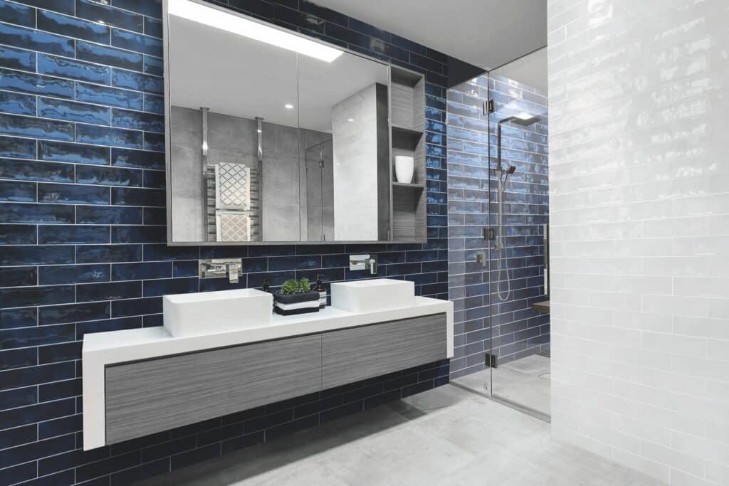A navy brick tiled bathroom wall behind twin basins and mirrors