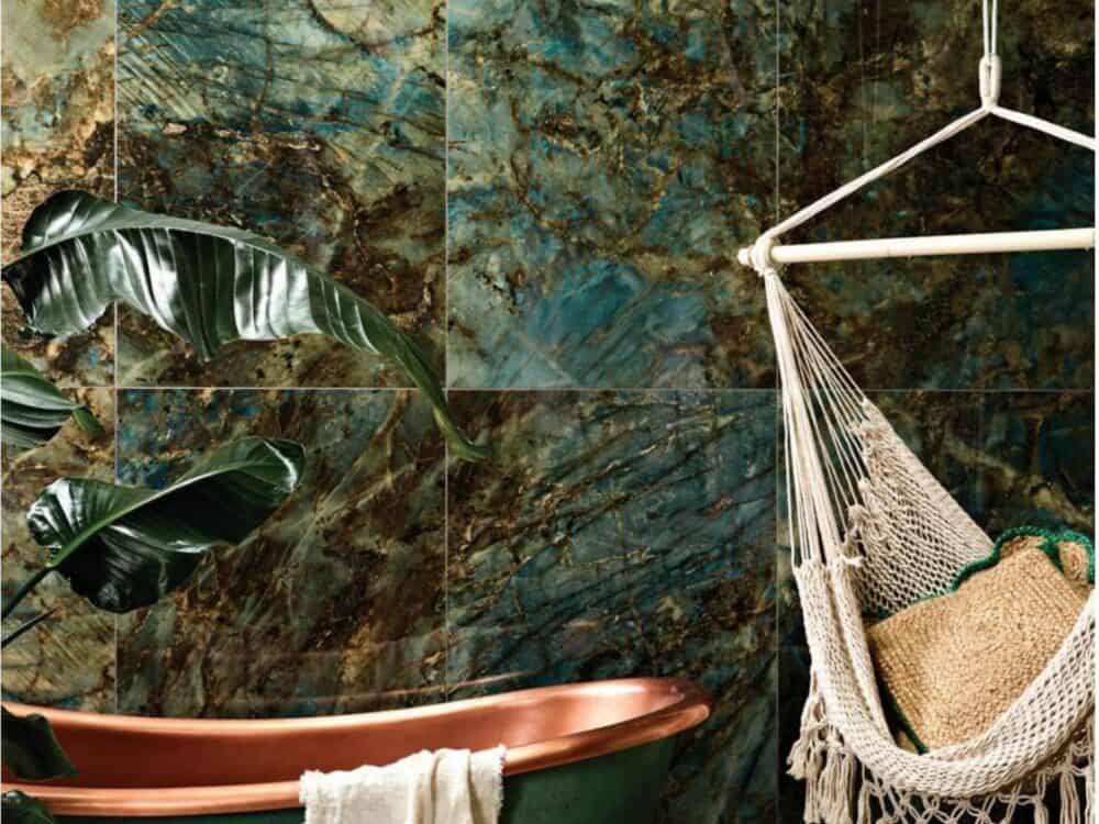 A green marble effect tiled wall beside a copper roll top bath