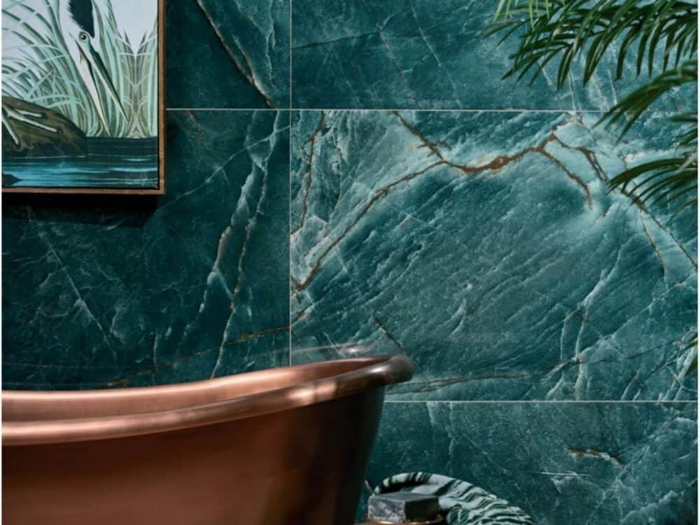 A jade green marble effect porcelain wall behind a copper bath