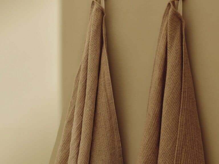 HiB brushed brass robe hooks with folded towels against an olive wall