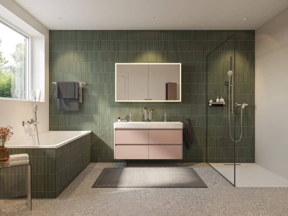 Laufen bathroom with a bath, pink vanity unit, illuminated mirror cabinet and walk-in shower against green tiles