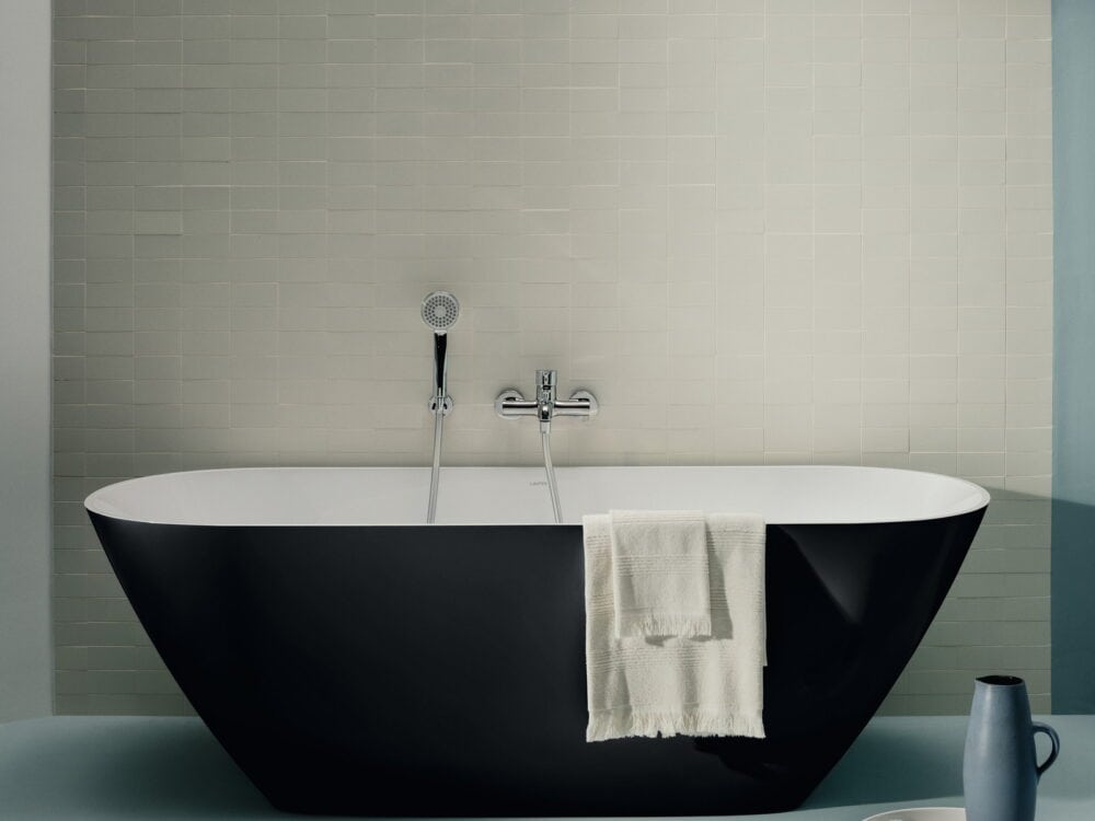 Laufen LUA black freestanding bath with a chrome bath filler against pale green tiles