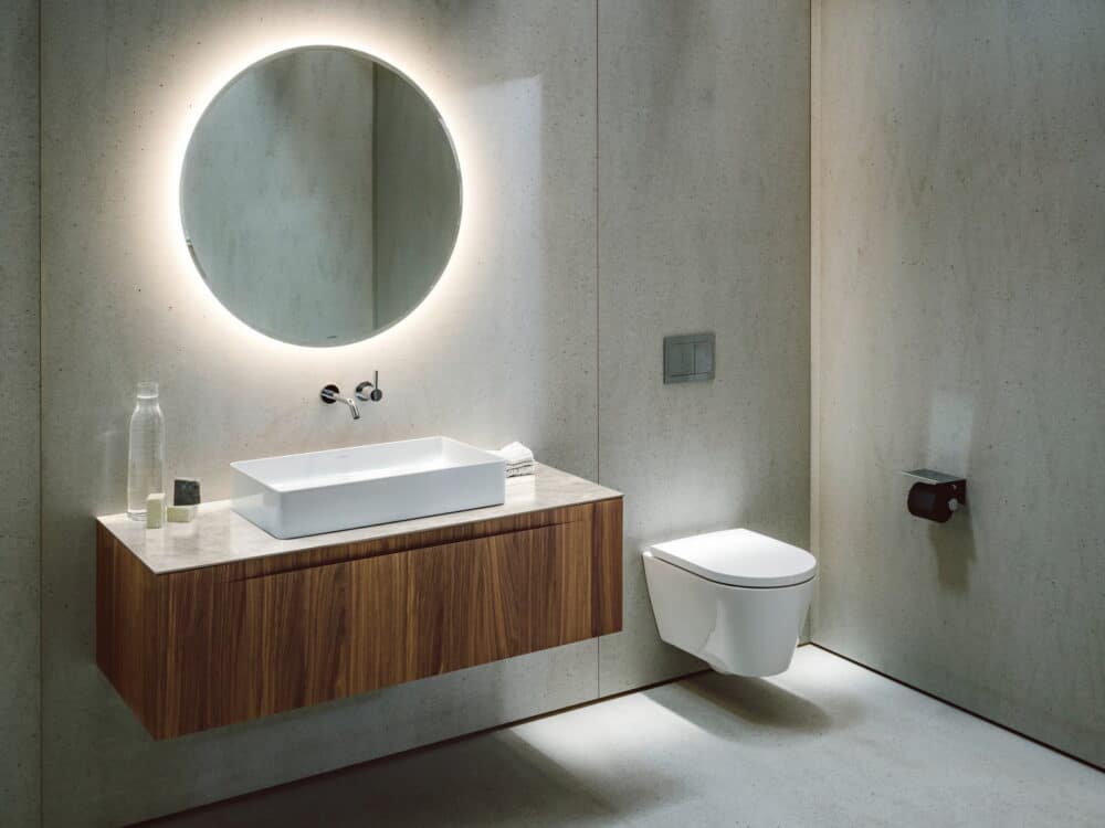 Laufen ARUN washbasin on a walnut vanity unit with a round backlit mirror and a wall-hung WC