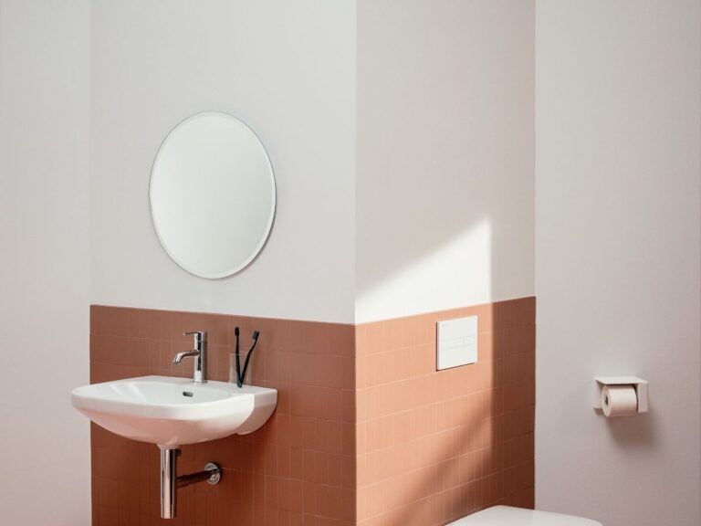 Laufen LUA round mirror above a wall-hung washbasin with terracotta wall tiles