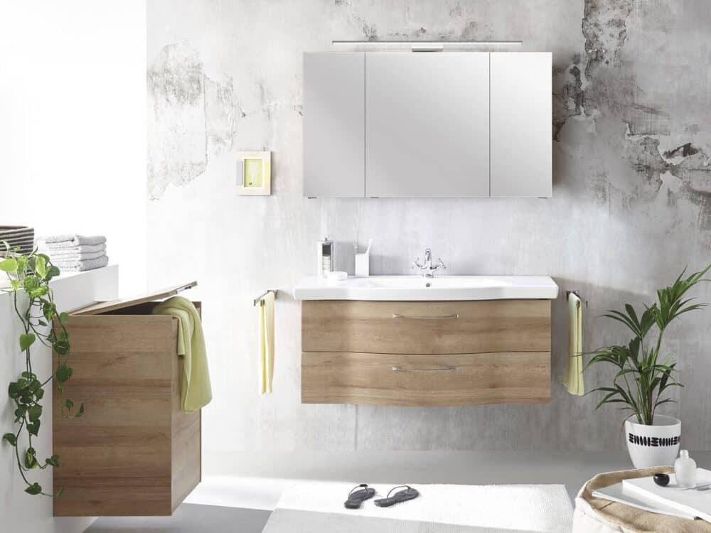Pelipal curved wood-finish vanity unit with a mirror cabinet against a concrete wall