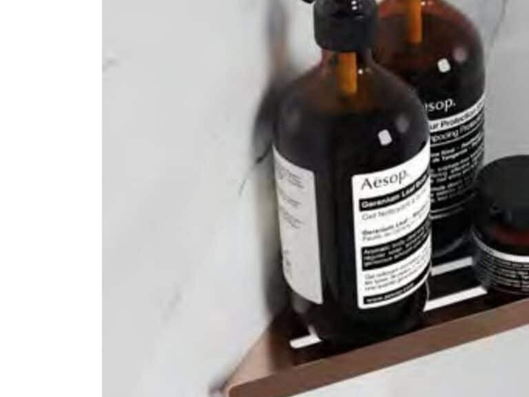 Phoenix brushed bronze bathroom shelf holding bottles against a marble wall