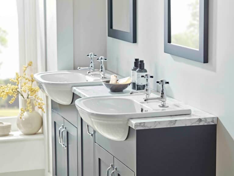 Two R2 Langford two tap hole basins set into a blue vanity run with a marble worktop beneath a window