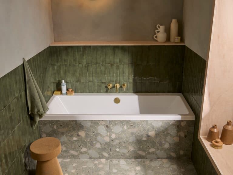 An R2 Serenity square double ended bath with brushed brass taps against a green tiled surround
