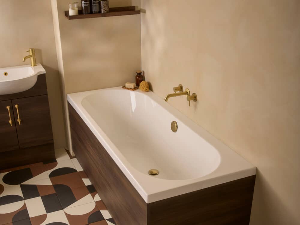 An R2 Sky double ended bath with brushed brass taps against a plaster wall and a chequerboard floor