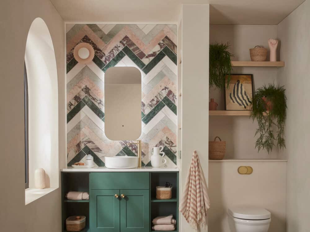 An R2 Stow fitted furniture run in Nordic green beneath an arched illuminated mirror and chevron tiles