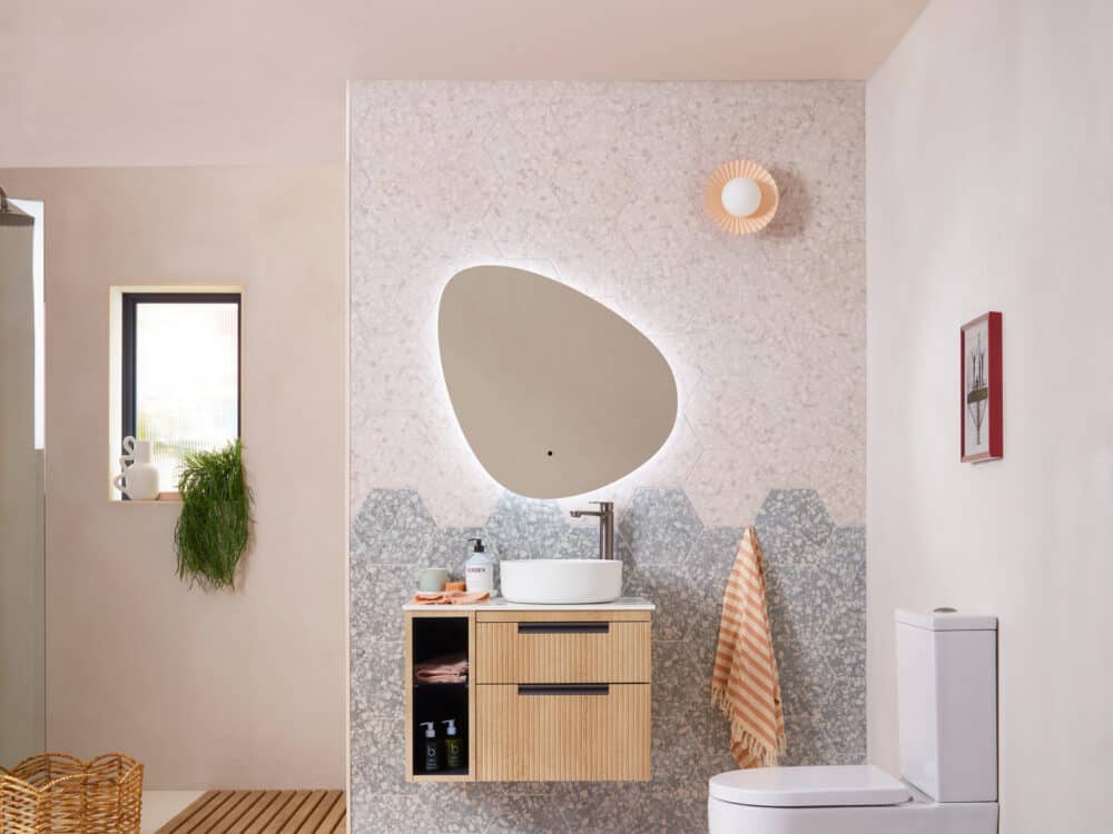 An R2 Platform 700mm fluted vanity unit in oak with a pebble shaped illuminated mirror against a blush wall