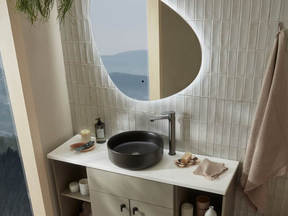 An R2 Pure Pebble illuminated mirror above a black countertop basin, with a window looking onto hills