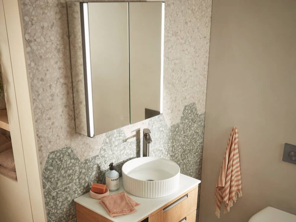 An R2 Flow mirrored cabinet above an oak Platform vanity unit and a terrazzo splashback
