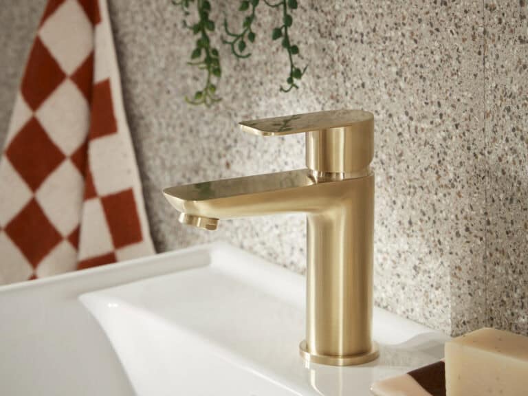 An R2 Crew basin mixer in brushed brass on a white basin against a terrazzo and red tiled wall