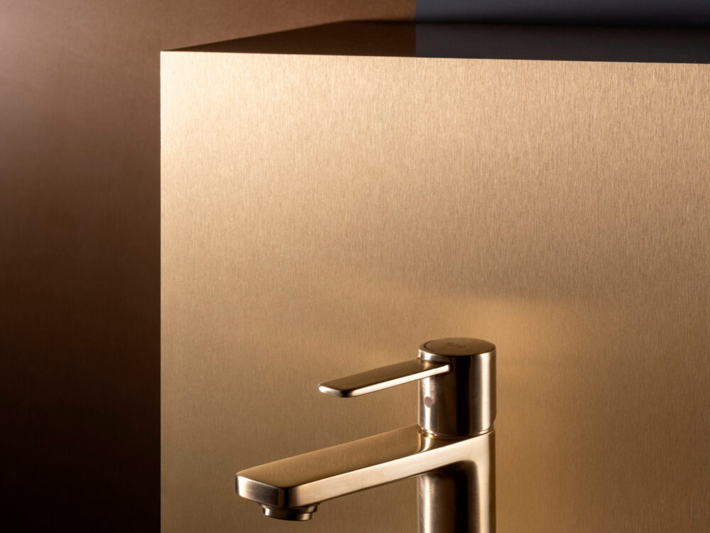 Roca Targa basin mixer in a brushed gold finish against a bronze backdrop