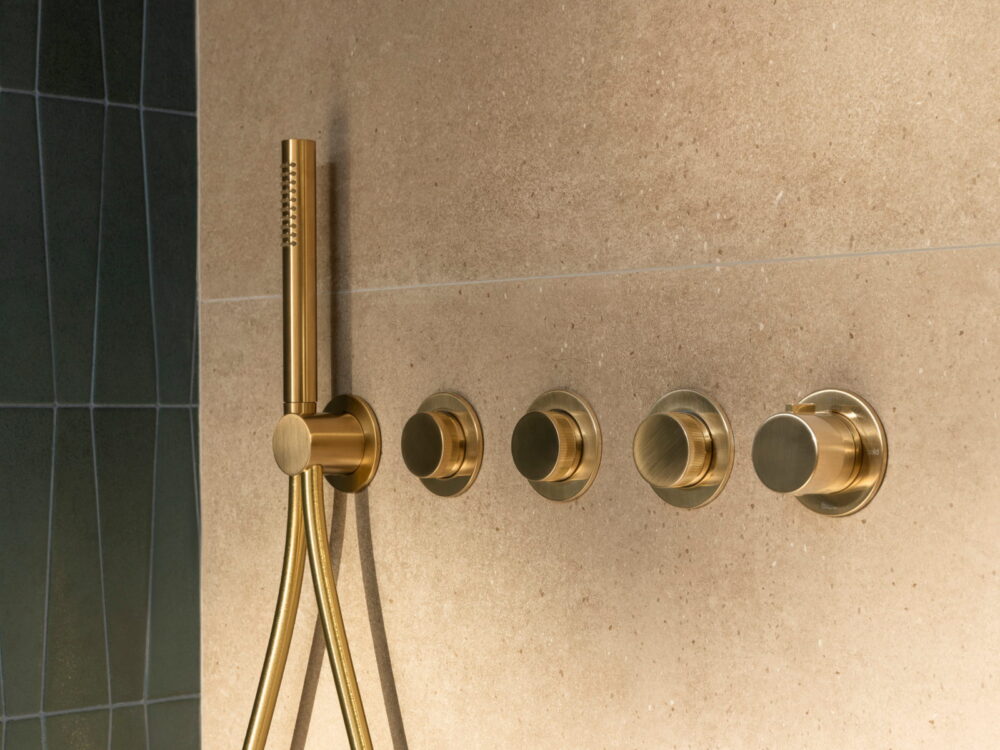 Roca brushed gold concealed shower valves and a slim handset on stone tiles