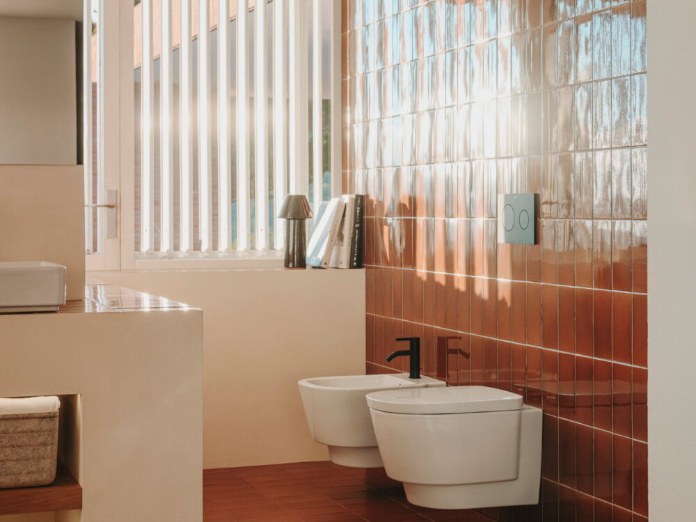 Roca Tura wall-hung WC and bidet beside a glass-block window in a terracotta-tiled bathroom