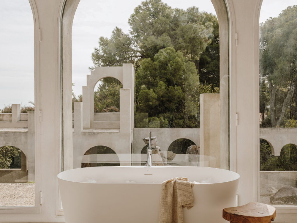 Roca Raina freestanding bath below an arched window with a stone courtyard beyond