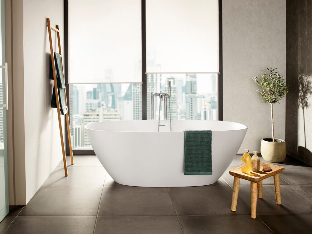 Roca Ariane freestanding bath with a floor-standing mixer in front of full-height city windows