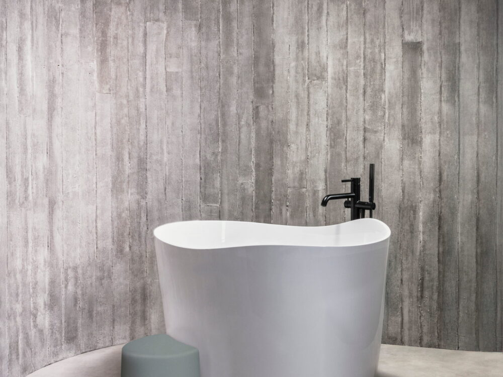 Roca Ohtake freestanding bath with a matt black floor-standing mixer against a board-marked concrete wall