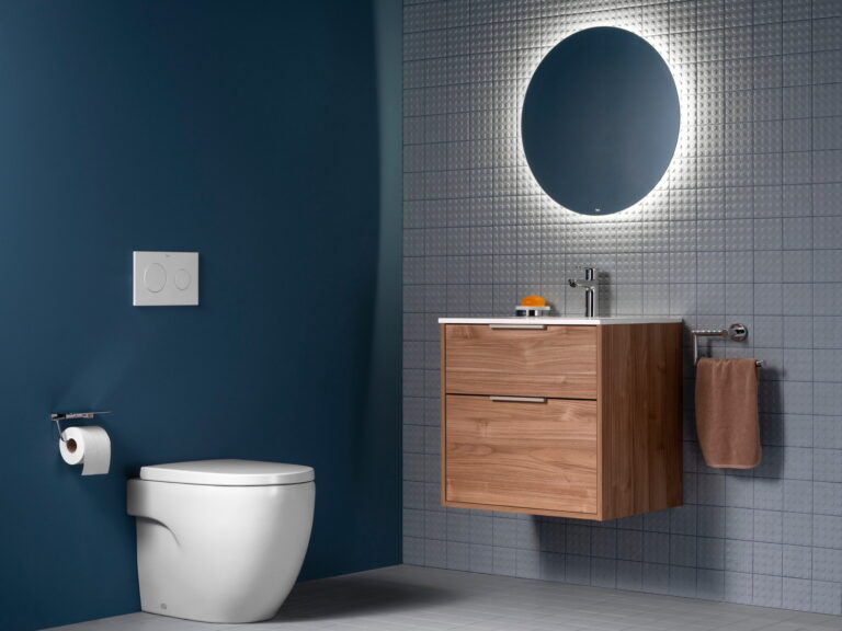 Roca Optica round backlit mirror above a walnut vanity unit, with a wall-hung WC against a deep blue wall