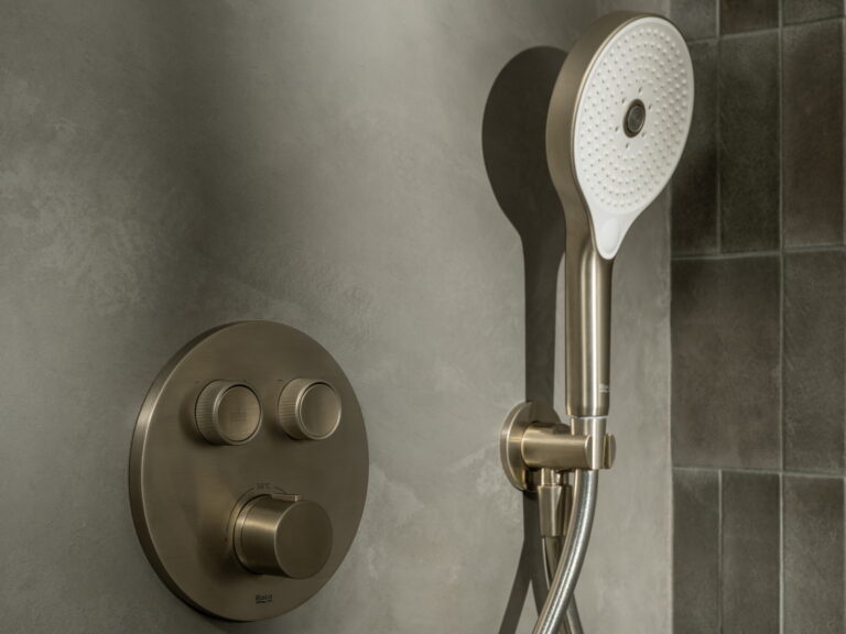 Roca T-3000 Round concealed thermostatic shower valve in brushed gunmetal with a handset on a grey stone wall