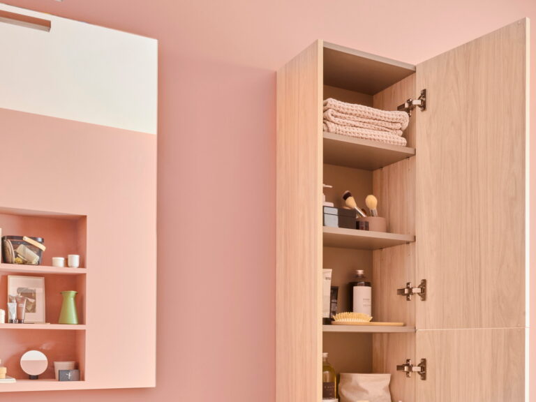 Roca Victoria-N oak tall cabinet standing open beside a recessed shelf unit on a dusky pink wall