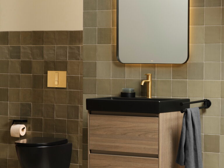 Roca brass-framed rectangular mirror above an oak vanity with a black countertop basin and matt black WC on olive tiles
