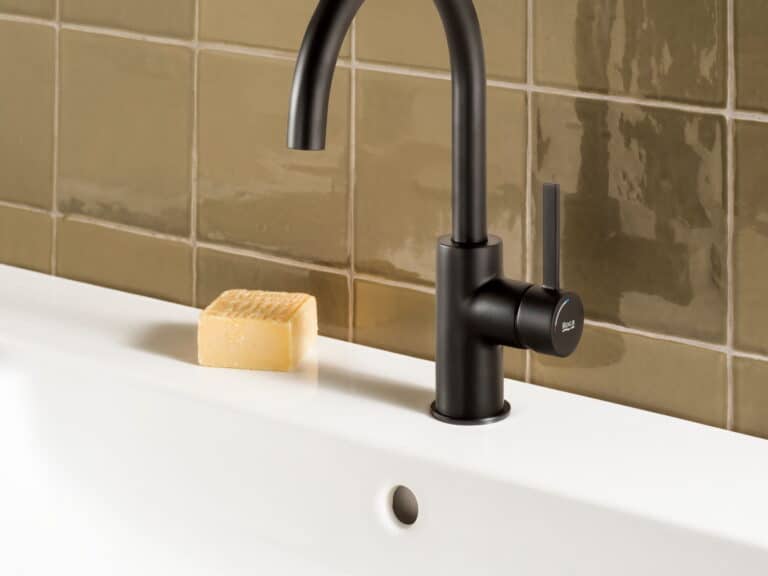 Roca Ona matt black basin mixer on a white washbasin against olive green tiles