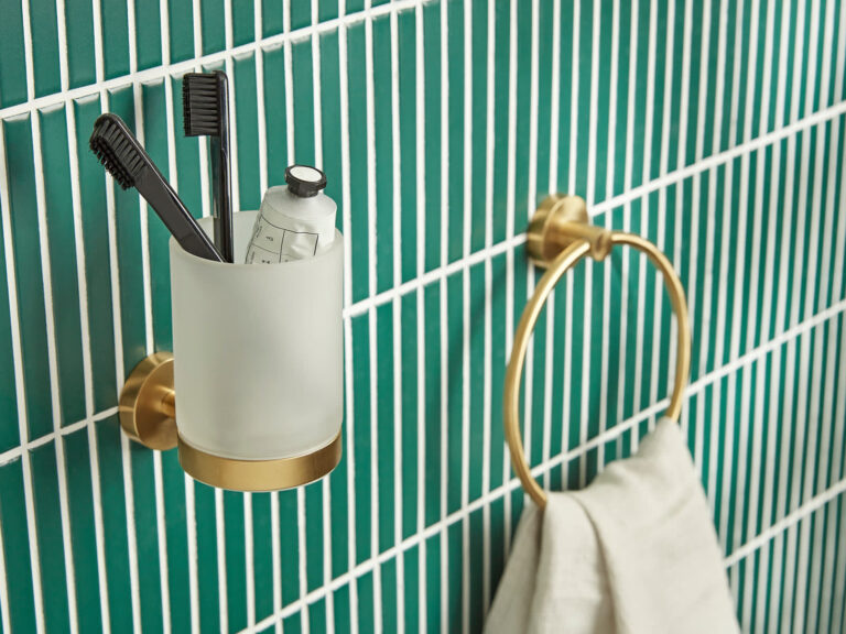 Roper Rhodes Capital brushed brass accessories, a tumbler holder and towel ring, on a green stacked tile wall