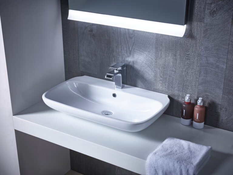 A Roper Rhodes Note 750 countertop basin on a grey worktop beneath an illuminated mirror
