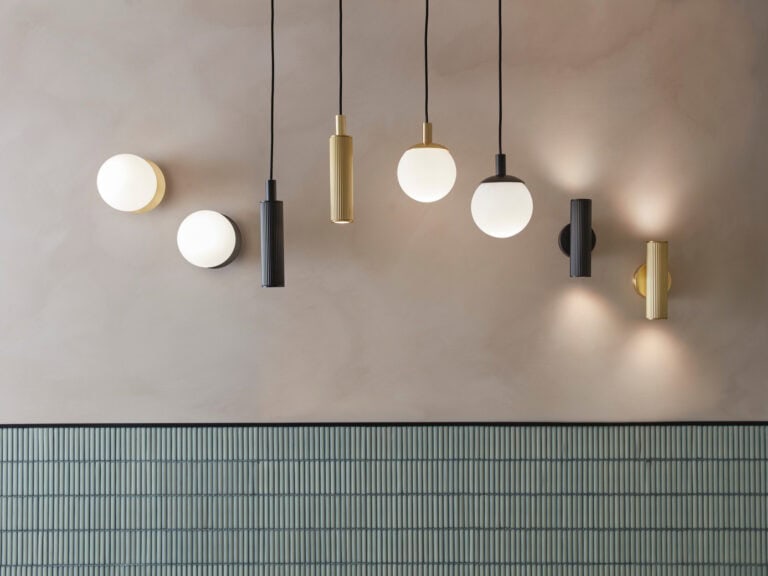 Roper Rhodes pendant and wall lights in black, brass and opal glass lit against a plaster wall above green tiles