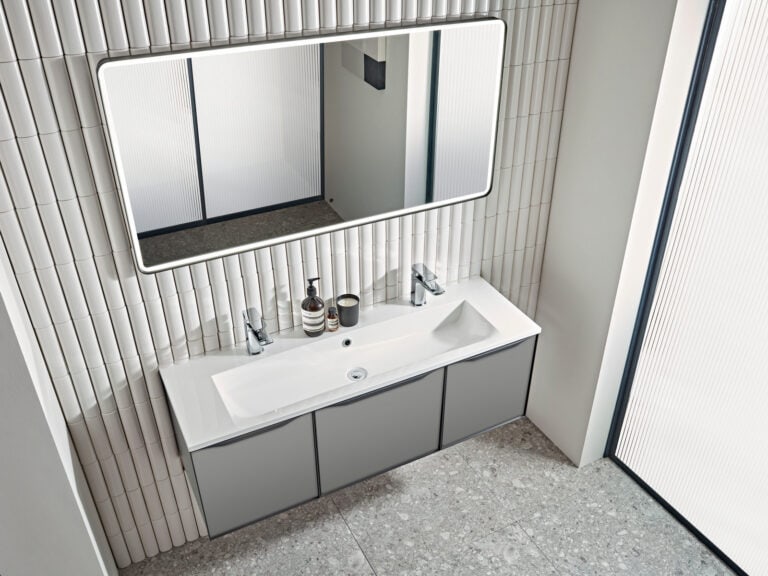 A Roper Rhodes Frame 1200 illuminated mirror lit above a wide double basin and a fluted wall