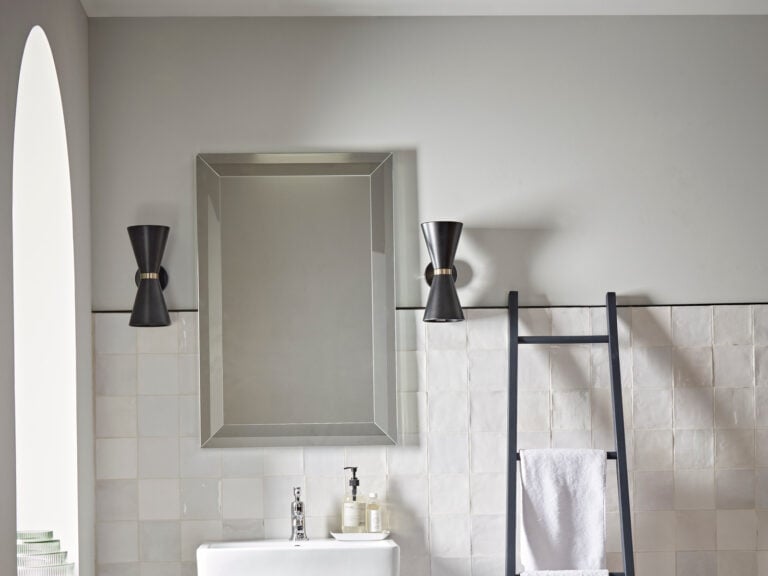 A Roper Rhodes Traditional bevelled wall mirror between two wall lights above a basin and white zellige tiles