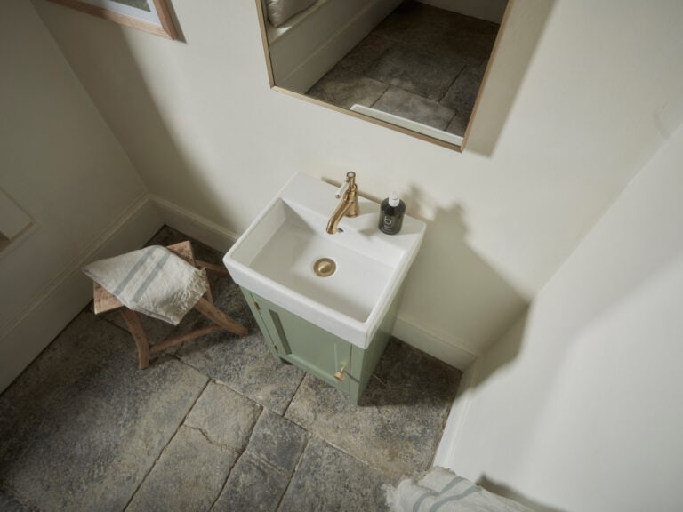A Roper Rhodes Hampton cloakroom unit in sage green with a brass tap, in a small slate-floored cloakroom